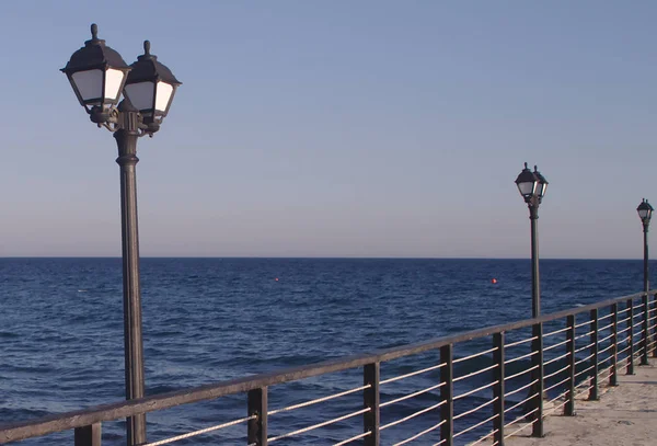 Row of street lights on a sea pier in front of the sky and the Mediterranean sea on blue hour