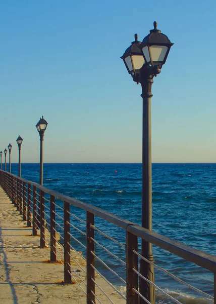 Row of street lights on a sea pier in front of the sky and the Mediterranean sea on blue hour