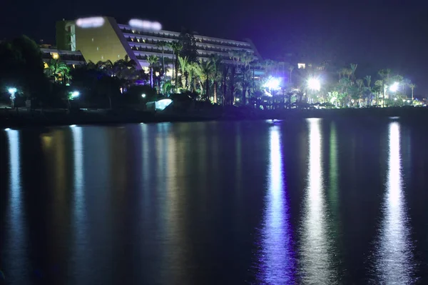 Bir plaj otelinin yakınındaki ışıklı bir sahilin renkli gece ışıklarının yansıması ile deniz suyu