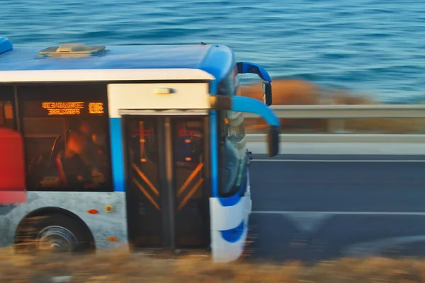 Mavi otobüs alacakaranlıkta sahil asfalt yol boyunca hızlı hareket