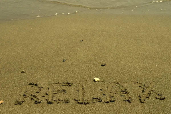Слово Relax Написано Мокром Желтом Песке Несколькими Камешками Перед Прозрачной — стоковое фото