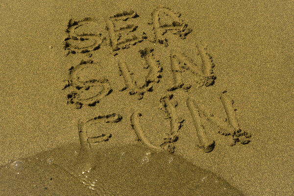 The words Sea, Sun, Fun written on the wet yellow sand close to the transparent rippled sea water at the summer beach
