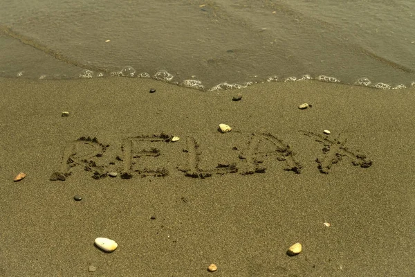 Слово Relax Написано Мокром Желтом Песке Несколькими Камешками Перед Прозрачной — стоковое фото