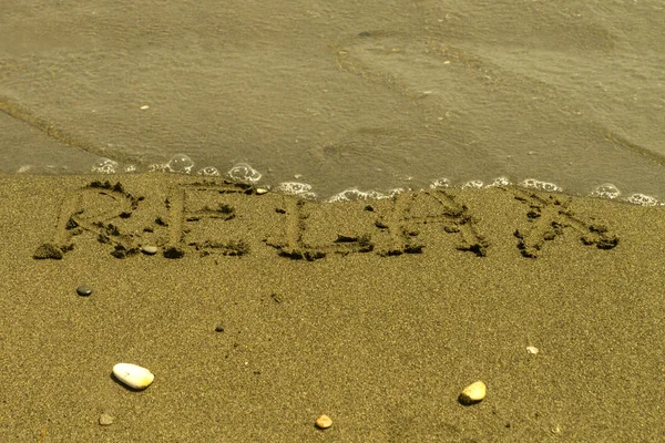 해변에서 거품과 잔물결 바닷물에 가까운 모래에 쓰여진 릴렉스라는 — 스톡 사진