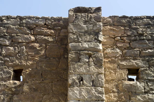 Close-up of an old ruined stone wall with two small holes and the clear blue sky above