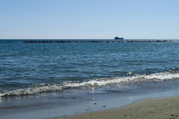 在阳光明媚的日子里 从明亮蓝色闪闪发光的大海的沙滩上欣赏着地平线上的一艘船 — 图库照片