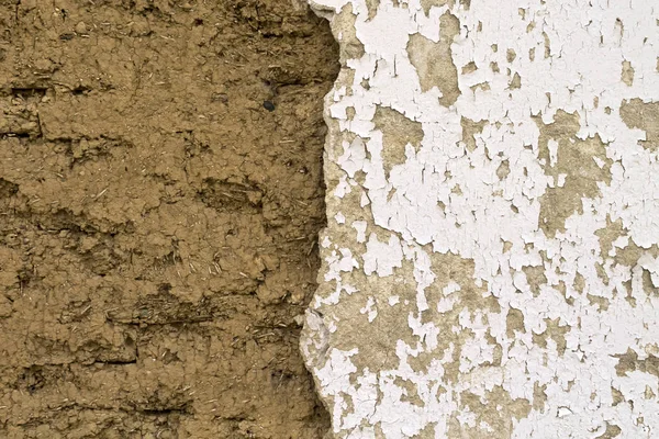 Part of an earth house wall half covered with old cracked plasterboard with peeling white paint