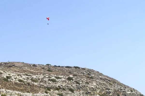 Kolorowy Paralotniarz Lecący Jasnoniebieskim Niebie Nad Skalistym Zboczem Góry — Zdjęcie stockowe