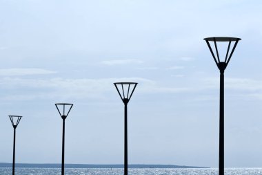 Siyah sokak lambalarının sıraları açık gri gökyüzünün ve parlak mavi denizin önündeki deniz önlerinde.