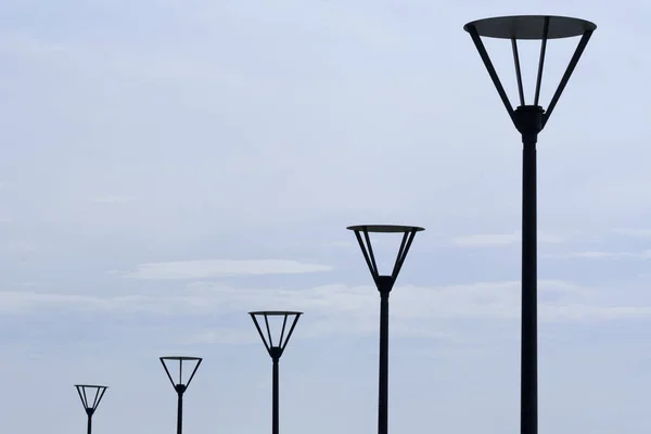 Row of the black street lamps in front of the pale gray sky