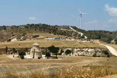 Tarımsal tarlaları, saman balyaları, yalnız kilise, yeşil tepeler ve rüzgar türbini kulesi olan kırsal alan