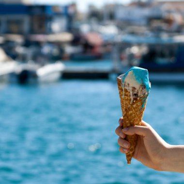 Erimiş dondurmalı waffle külahı, bulanık mavi denizin önünde. 