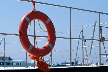 Mavi gökyüzünün önündeki korkuluklarda turuncu can simidi