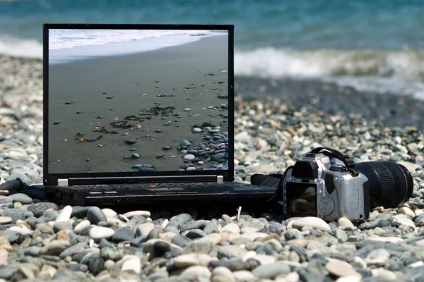Laptop and camera laying on Cypriot beach among gray pebbles in front of the sea