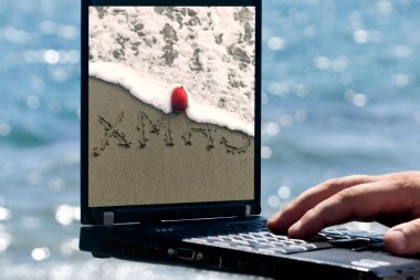 Mavi denizin önündeki monitöründe kelime ve kırmızı Noel topu resmi olan bir dizüstü bilgisayar.
