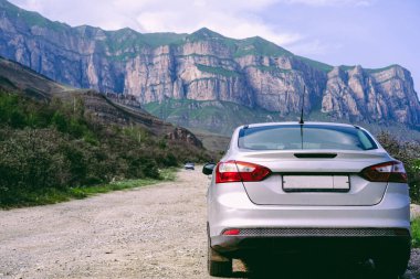Araba, dağların arka planına karşı yolda duruyor.