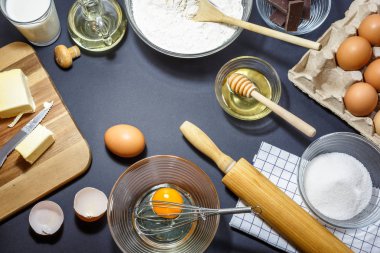 Mutfak gereçleri ve kek pişirme için malzemeler. Yumurta, un, yağ, tereyağı, süt, bal, şeker ve çikolata koyu arka plan üzerinde. Fırın kavramı, yüksek açıdan görünümü.