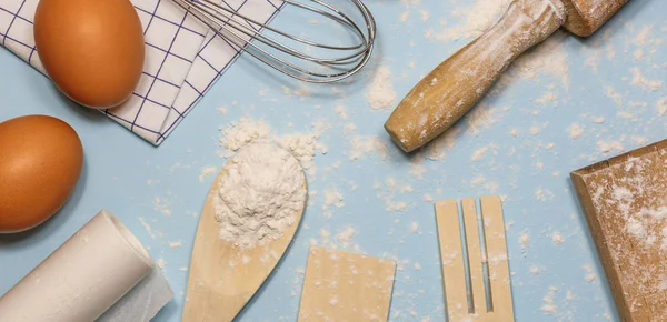Ingredients and kitchen items for baking cakes. Kitchen utensils, flour and eggs on light background, top view.
