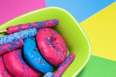 Mavi ve pembe sırlı çörek çikolata ve şeker çubukları kase renkli arka plan üzerinde yakın çekim görünüm seçici odak ile.