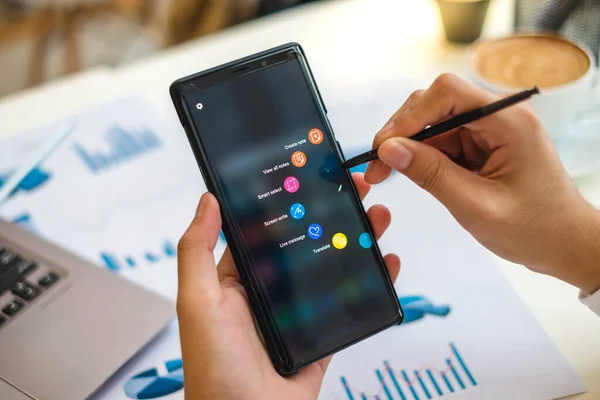 RAYONG THAILAND - 20 Ekim 2018 Samsung Galaxy Note9 'un kalem tutan işadamlarının ellerini kapat ve masa başında çalışırken aygıt ekranında kısayol simgeleri göster.