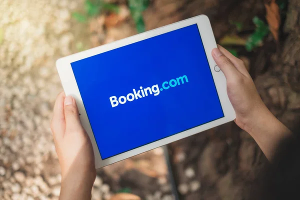 RAYYONG, THAILAND, APR 12.2020: Elma Ipad 'i tutan Asyalı adam tatil için uçak ve otel rezervasyonu yapmak için Booking.com uygulamasını kullanıyor.