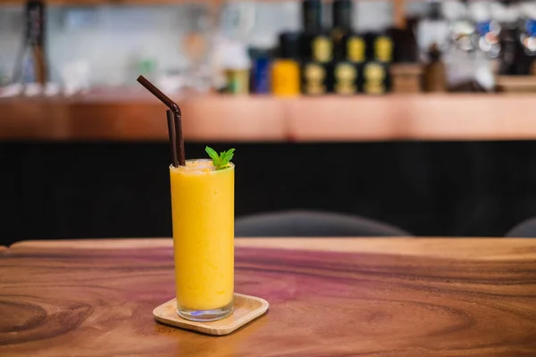Bir bardak Mango Smoothie, ferahlatıcı içecekler, ahşap masada servis edilir..