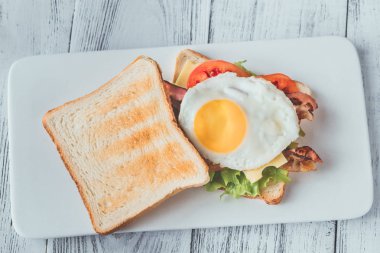 Beyaz tabakta kızarmış yumurta ve pastırmalı sandviç.