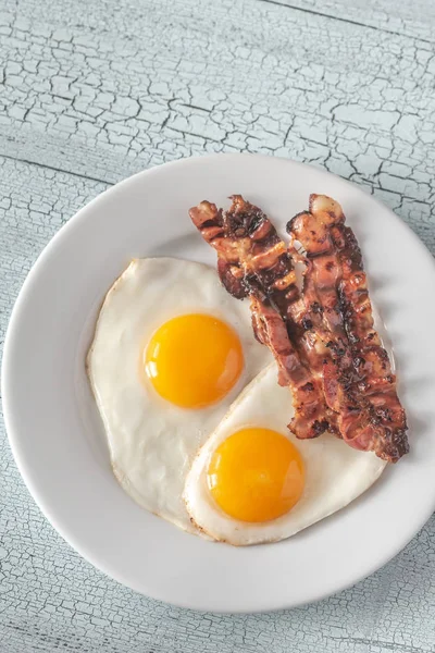 Жареные яйца и бекон на белой тарелке — стоковое фото