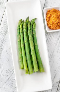 Beyaz servis tabağında romesco soslu haşlanmış kuşkonmaz.