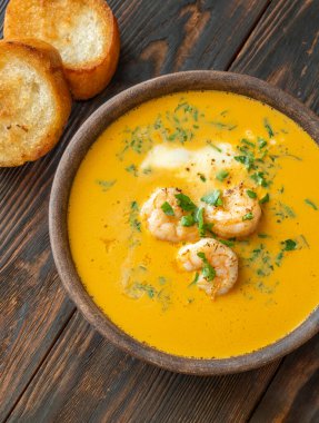 Shrimp bisque in rustic clay bowl, served alongside toasted golden baguette slices
