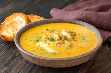 Shrimp bisque in rustic clay bowl, served alongside toasted golden baguette slices