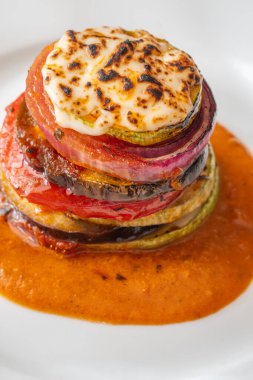 Baked ratatouille vegetables stacked in a vibrant tower, golden layers highlighted beautifully