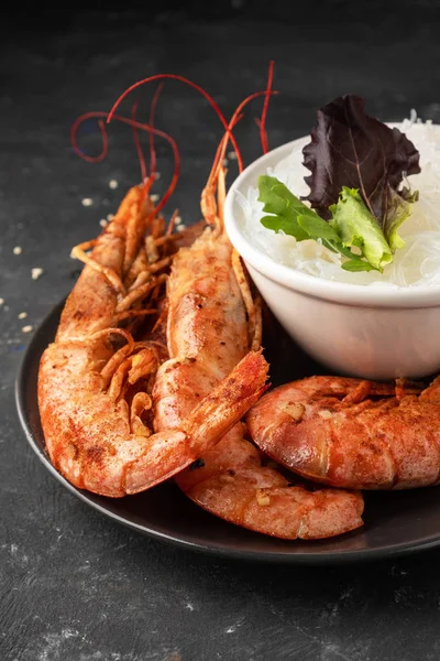 Fried grilled prawns with rice noodle and lettuce leaves, dark background, copy space