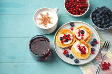 Kırmızı frenk üzümü ve yaban mersini ile süzme peynir krep. Mavi arka planda kahve, meyve suyu, çilek ve sos. Taze ve lezzetli kahvaltı.