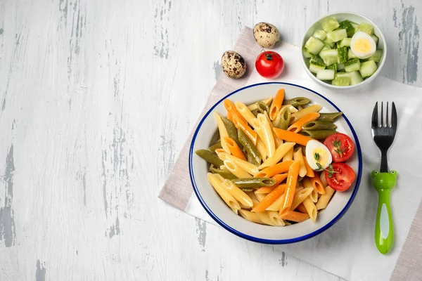 Açık ahşap arka plan üzerinde bir tabakta çok renkli penne makarna, çocuk için bir yemek. Çocuk menüsü. Üst görünüm, kopyalama alanı, yakın çekim.
