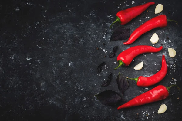 Red hot chili peppers on a black background. Hot spicy spices for cooking: chili pepper, garlic, basil. Copy space.