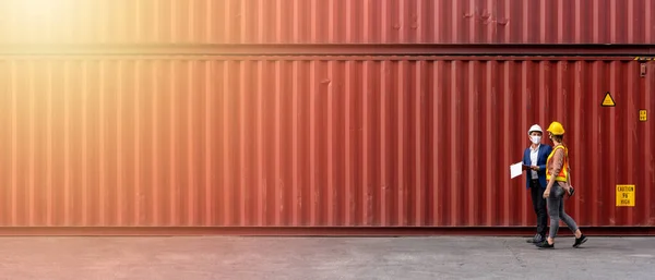 Ulaşım ve lojistik işi kavramı, liman nakliyatında konuşan iki teknisyen, Foreman ve rıhtım işçisi, sanayi konteynır sahasında 21: 9 'da yürüyen sert şapkalar giyiyorlar.