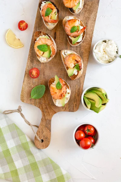 Bruschetta italian snack sandwiches with shrimps, avocado and cheese decorated by basil.