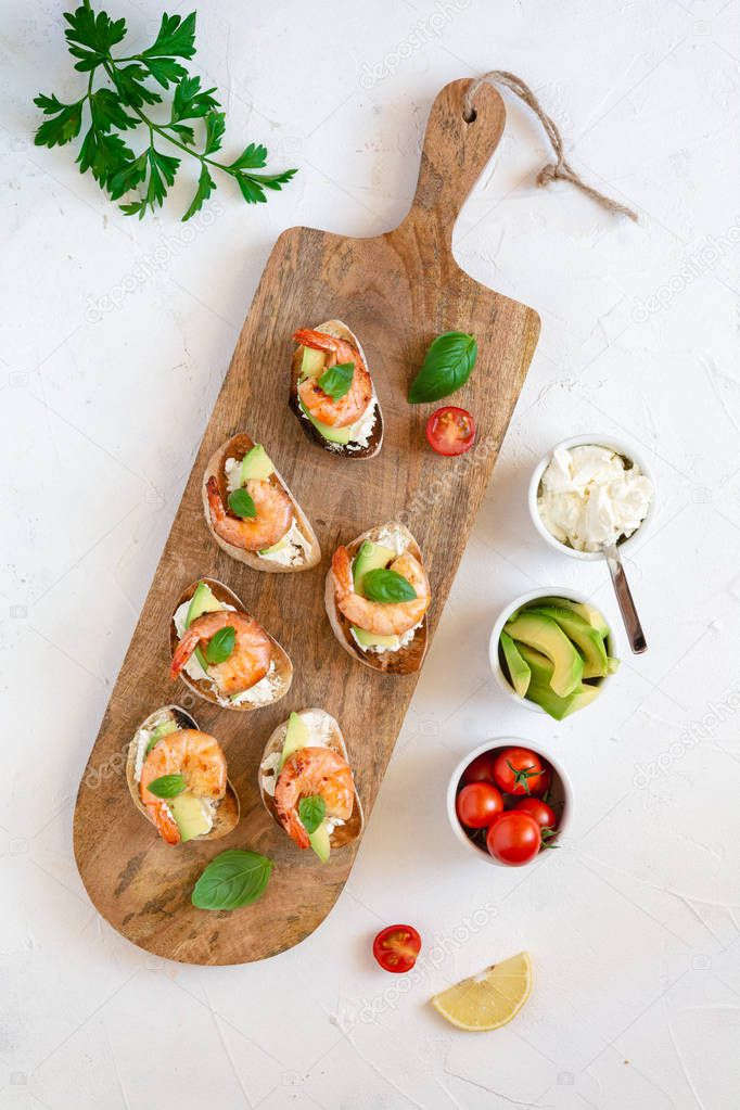 Bruschetta italian snack sandwiches with shrimps, avocado and cheese decorated by basil.