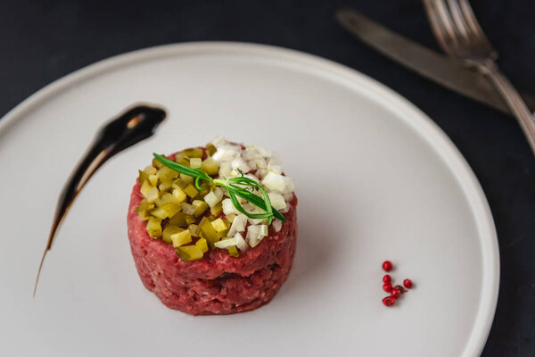 Beef tartare with pickled cucumber and fresh onion on plate.