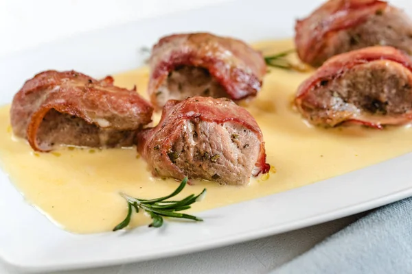 Baked pork tenderloin wrapped in bacon served in a cheese sauce with rosemary