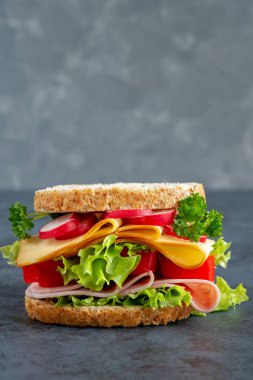 Jambon, peynir ve karanlık bir arka plan üzerinde taze sebze ile Graham ekmek sandviç. Kahvaltı kavramı. Jambon, peynir ve karanlık bir tahta üzerinde taze sebze ile sağlıklı sandviç. Kahvaltı konsepti.