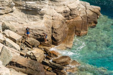 : Sifnos, Yunanistan - 11 Eylül 2018: deniz su ile çevrili bir kayanın üzerinde duran bir çift. Ege Denizi