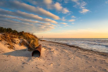 Kumlu sahilde günbatımı ışık büyük eski paslı boru. Hel yarımadasında. Polonya
