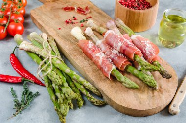 Prosciutto jambonu bir kesme tahtası üzerinde sarılı taze organik kuşkonmaz.