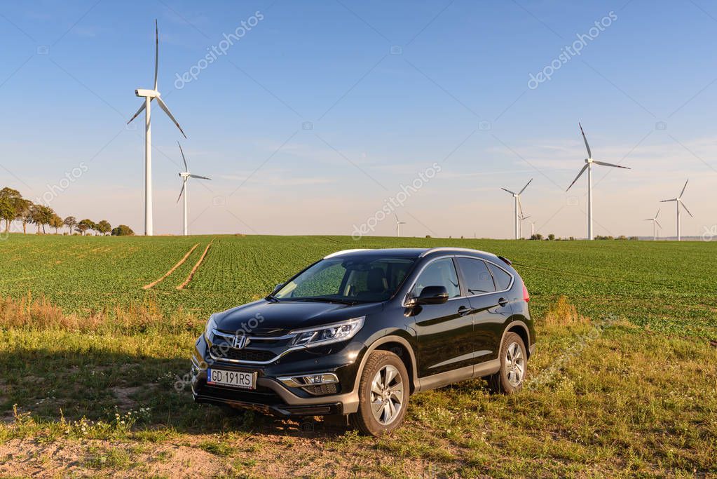 PUCK, POLAND - September 18, 2018: Honda CR-V car parked in a field on a country road next to a wind farm