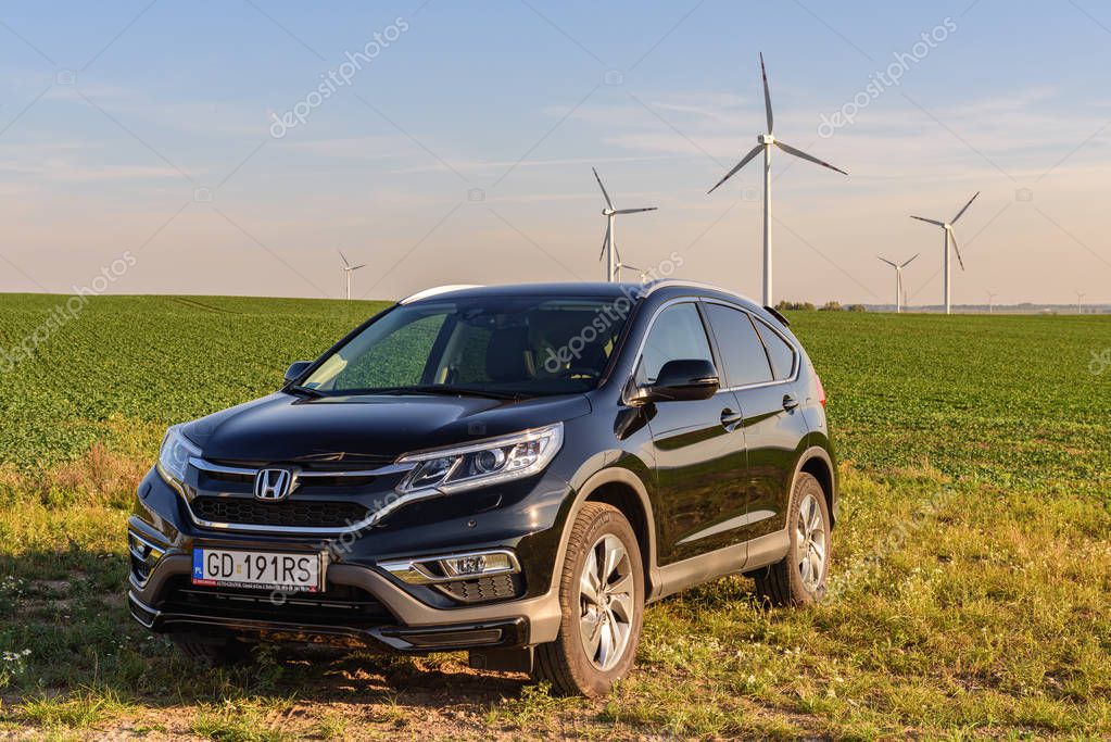 PUCK, POLAND - September 18, 2018: Honda CR-V car parked in a field on a country road next to a wind farm