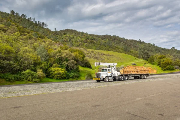 CALIFORNIA, EE.UU. - 4 de abril de 2019: Camión grande con letrero de carga ancha y remolque de bajada que transporta madera . —  Fotos de Stock