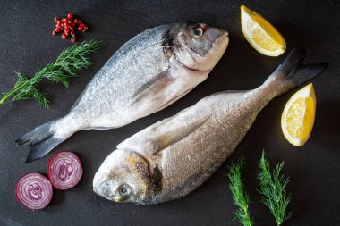 Siyah tabakta servis edilen sebzeli taze pişmemiş dorado balığı.