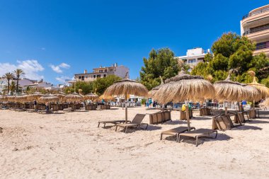 Mallorca, İspanya - 6 Mayıs 2019: Mallorca'nın kuzeybatısında popüler bir aile tatil beldesi olan Port de Pollenca'da (Puerto Pollensa) sahilde saman şemsiyeler. İspanya